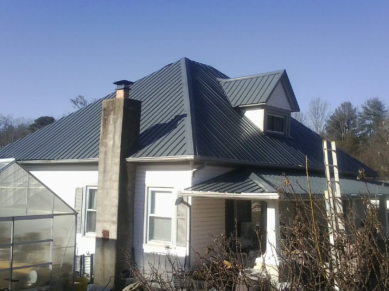 Dark blue standing seam metal roof on a white farmhouse with dormer — Slate & Tile Roof Repair by Roofing Brothers in Markham