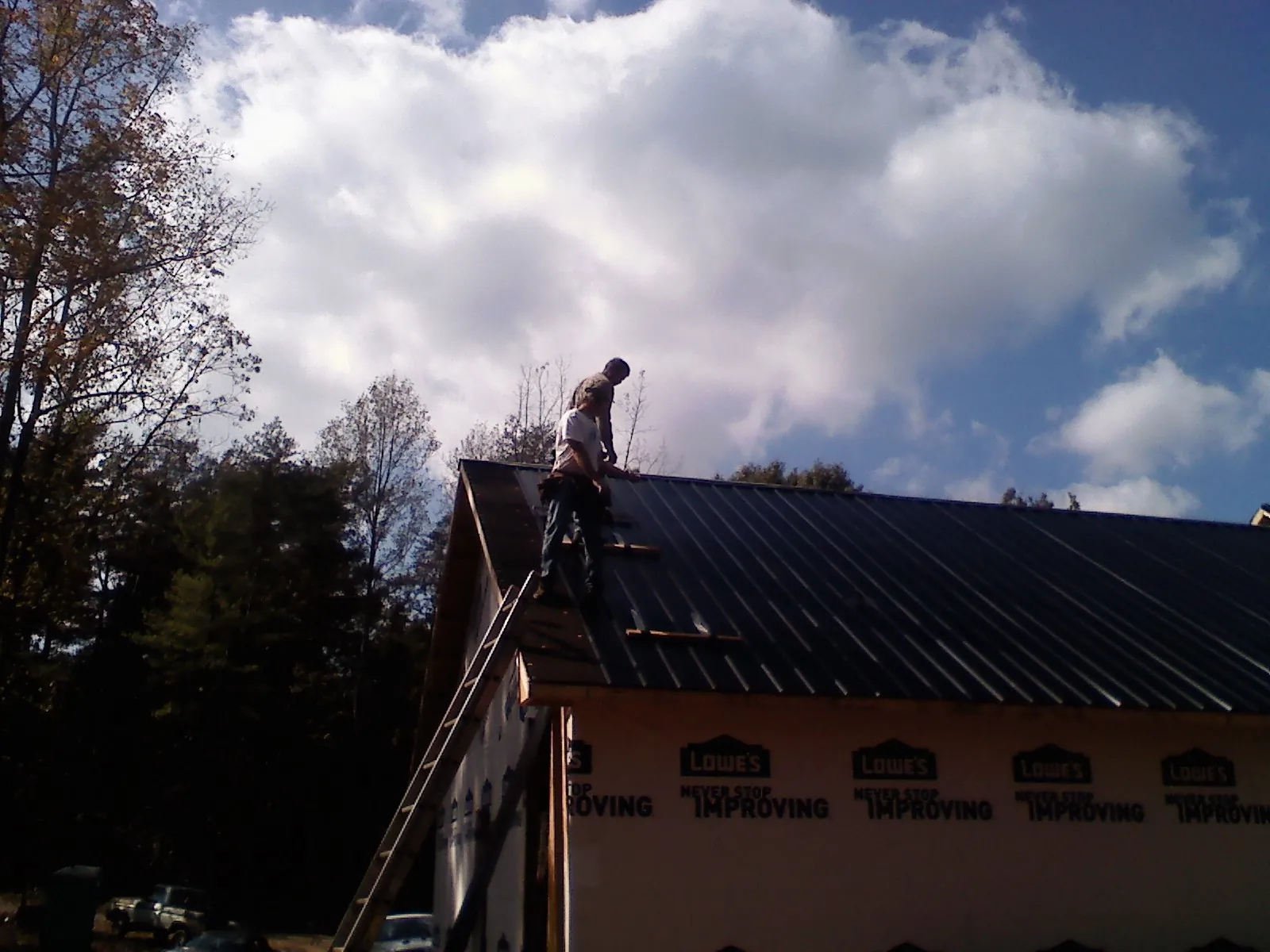 Roofer fastening dark metal panels high against a cloudy sky, from a Roof Inspection job in Markham